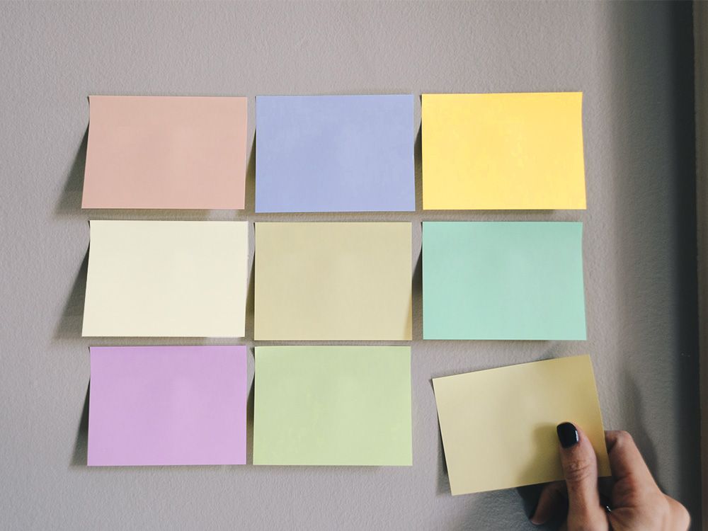 Leere Post-it-Zettel, die in einem 3x3 Muster an einer grauen Wand hängen
