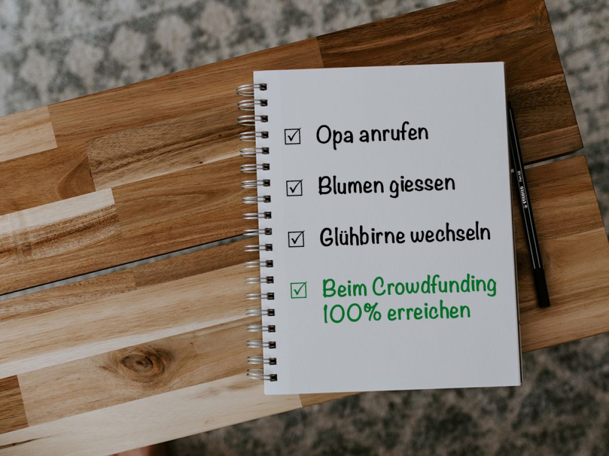 Sicht von oben auf einen Notizblock und einen Stift auf einer schmalen Holzbank. Auf dem Notizblock steht die To-Do Liste "Opa anrufen, Blumen giessen, Glühbirne wechseln, Beim Crowdfunding 100% erreichen"